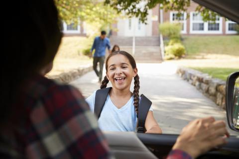 年轻的女孩用父母的汽车奔跑，在她的学校外面的脸上微笑。