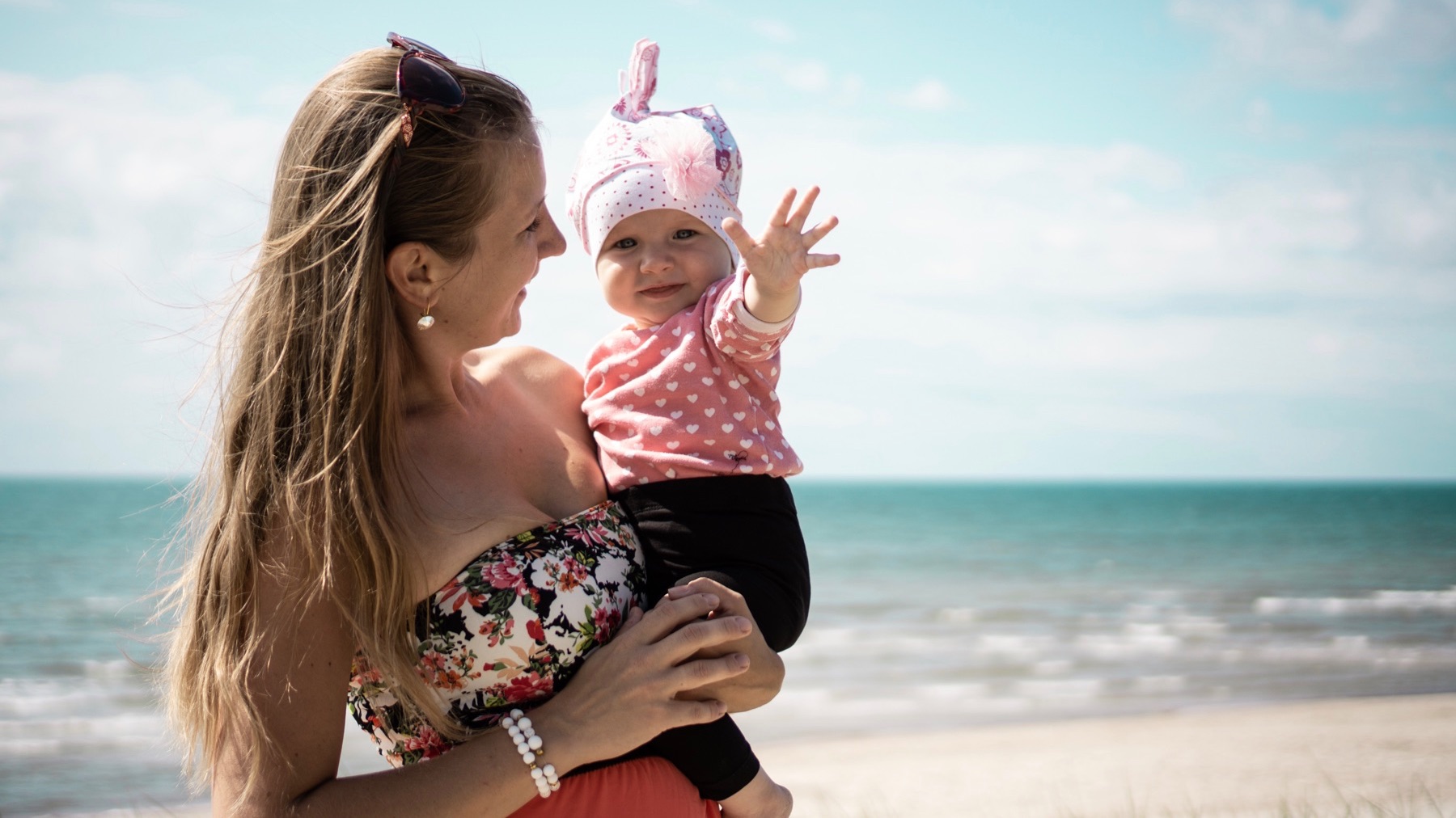 一个女人微笑，因为她抱着一个婴儿在海洋附近的海滩上。