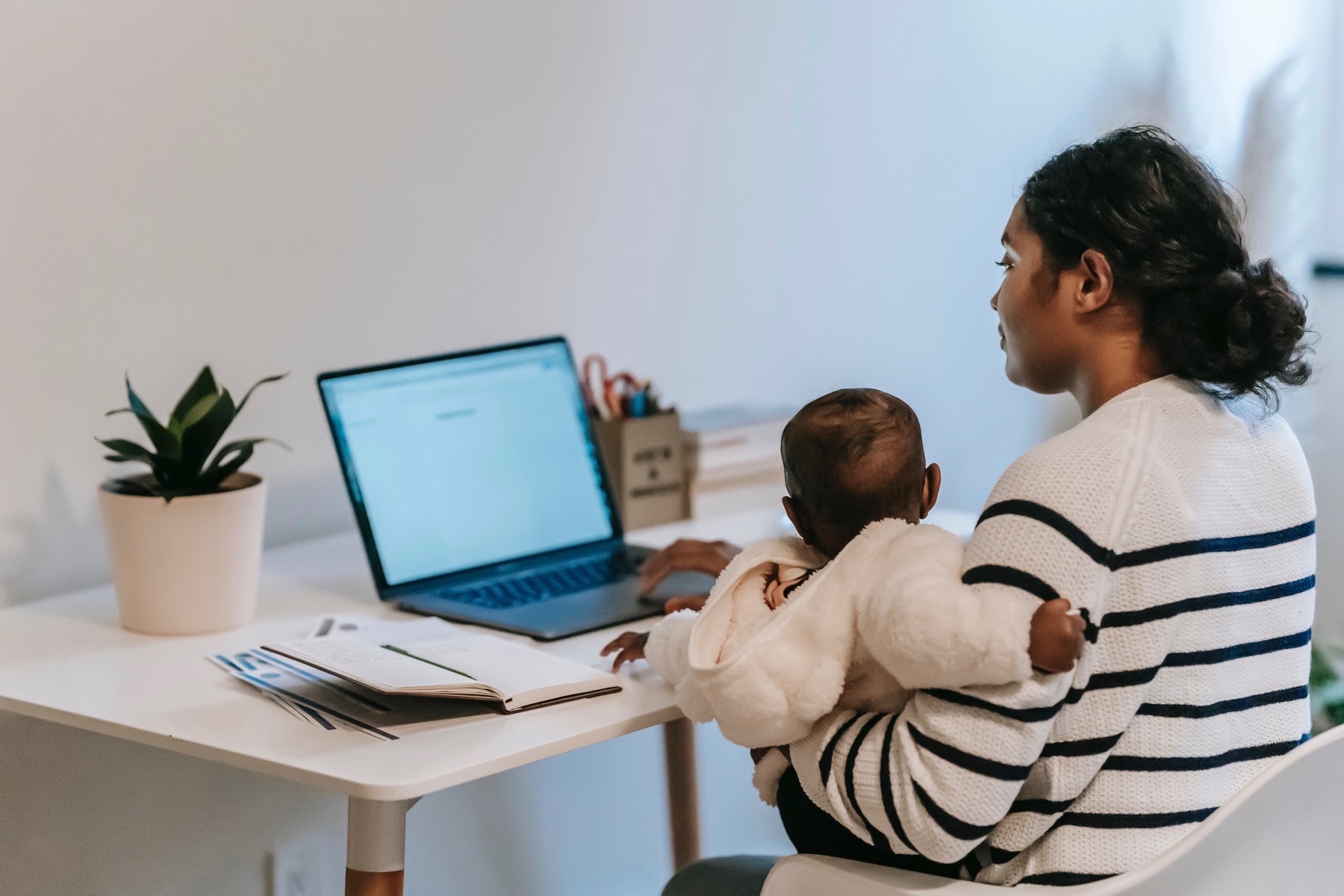 母亲在她的桌子上使用笔记本电脑时抱着婴儿。