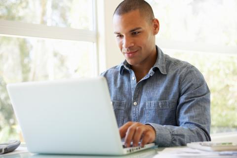 一名男子坐在桌前使用笔记本电脑