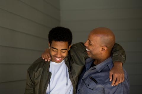 少年儿子和父亲站立笑，搂着彼此的肩膀
