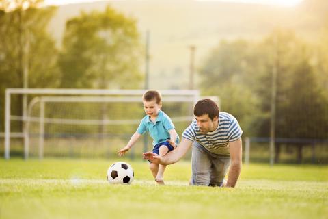 一个男人和一个小男孩在操场上踢足球。