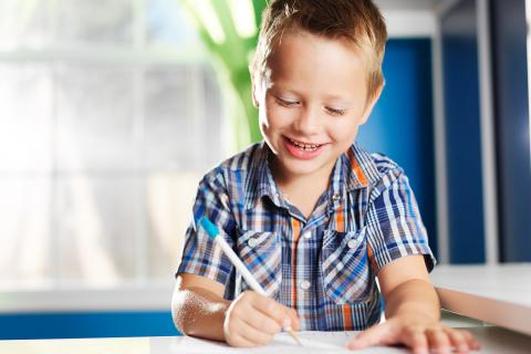 笑容满面的孩子坐在书桌前，在一张纸上写字。