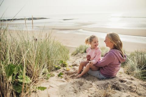 女儿坐在母亲的膝盖上，因为他们在海滩上放松。