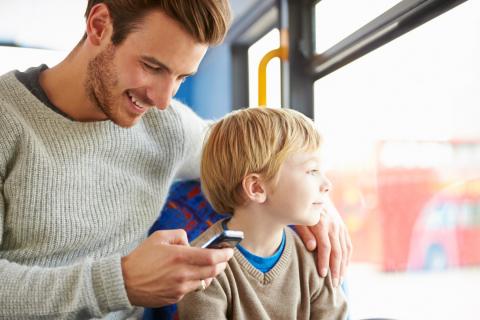一位父亲在和儿子乘坐公共汽车时看手机。