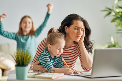 一位忙碌的母亲看着她的电脑，她的孩子们在她周围玩耍。