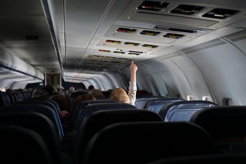 小男孩坐在飞机上，伸手去拿头顶上的灯。