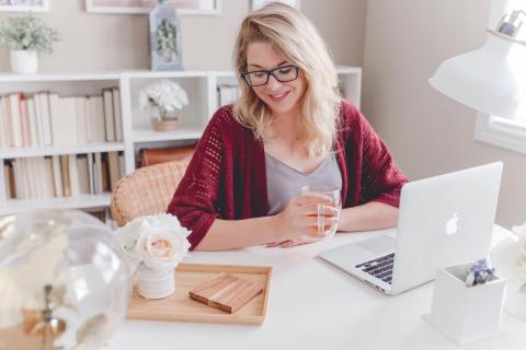 一位女士一边喝茶一边低头看着电脑，面带微笑。