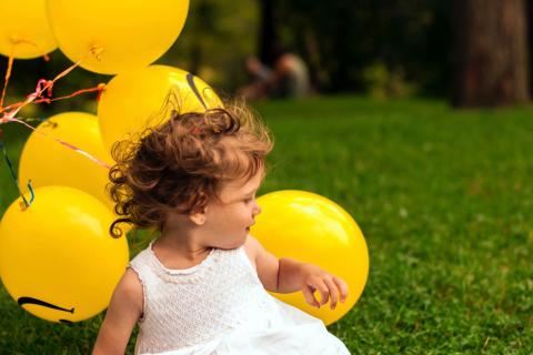 女孩坐与一束黄色气球的草
