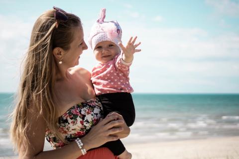 一位妇女在海边的海滩上抱着一个婴儿，微笑着。