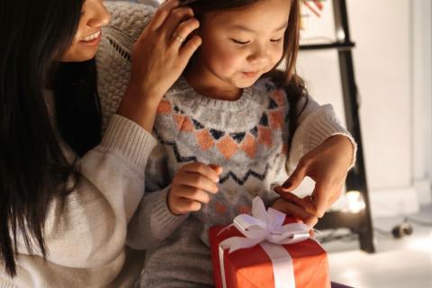 一个年轻的女孩坐在她的母亲的膝盖上，因为她收到假日礼物。