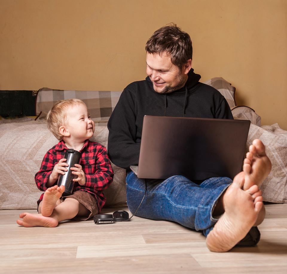 父亲在笔记本电脑上工作，年幼的儿子快乐地坐在他身边。